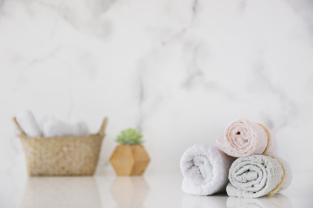 Rolled white towels, a woven basket and a small plant on a marble counter